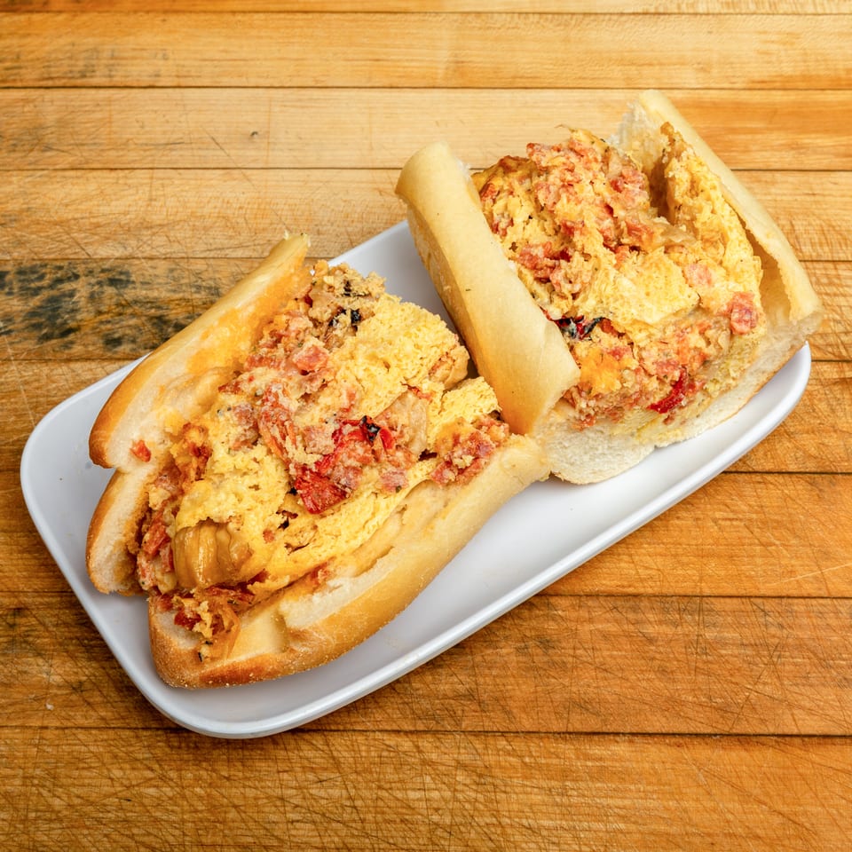 Two stuffed seafood sandwiches with creamy lobster filling and red peppers on a white plate atop a wooden cutting board.