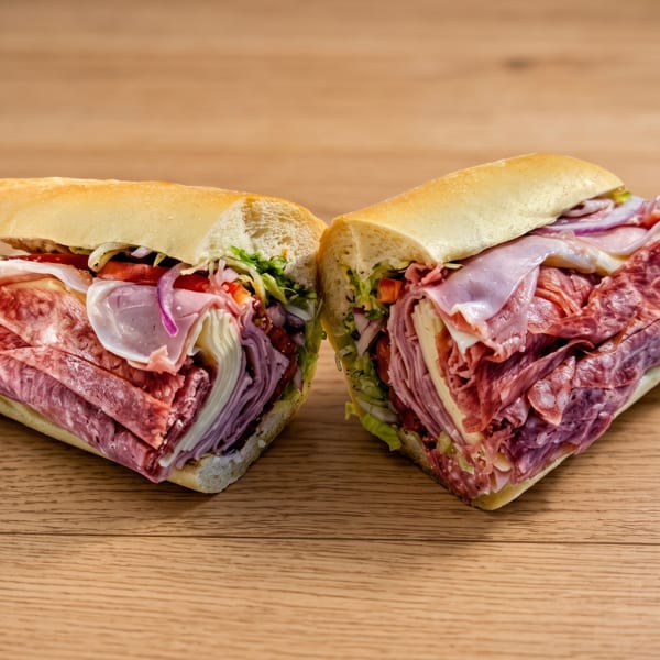 Two halves of a large deli sandwich, packed with various meats, cheese, and vegetables.